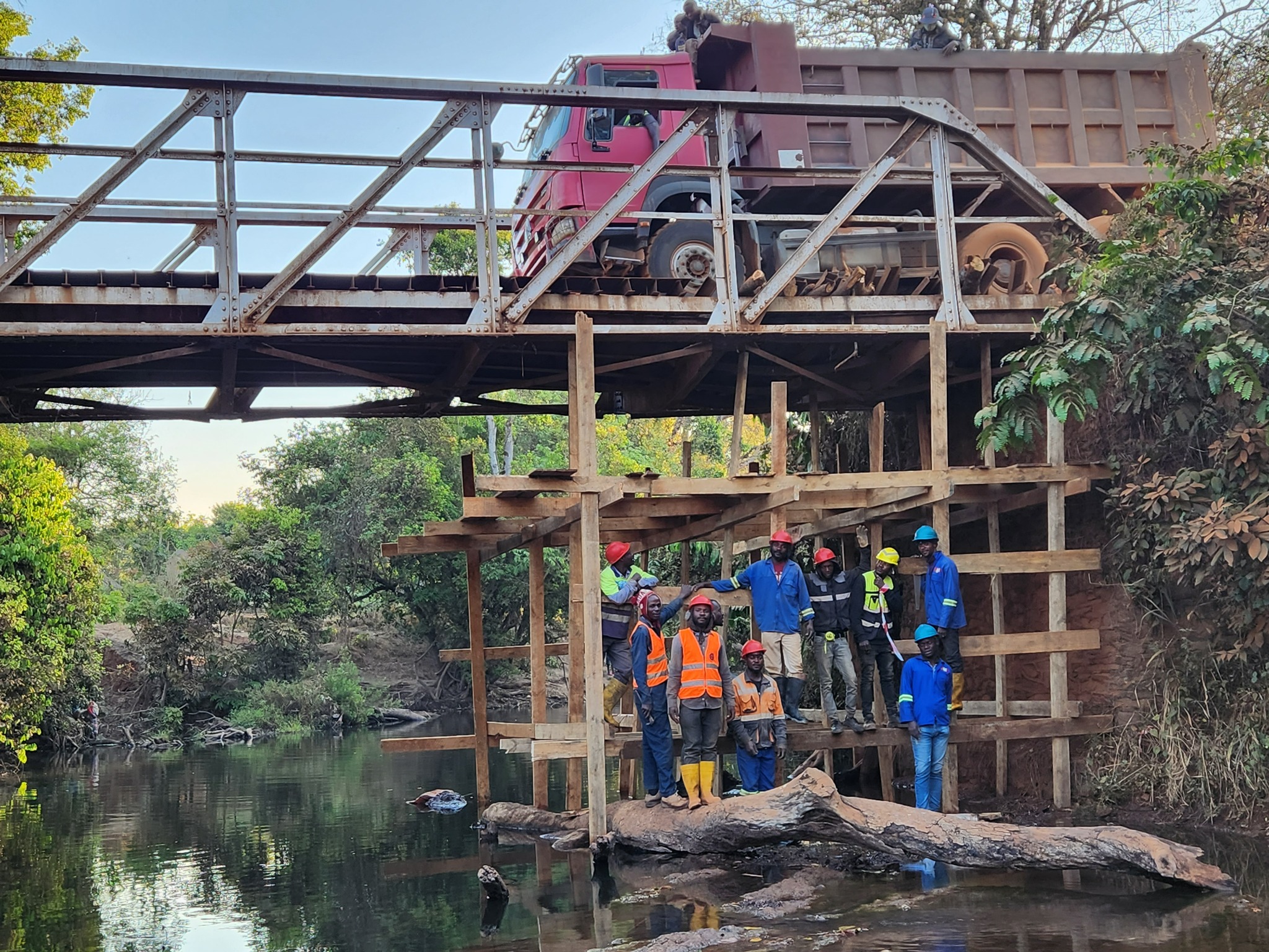 Vue latérale du pont, structure en bois sous l’ouvrage et équipe au bord du cours d’eau